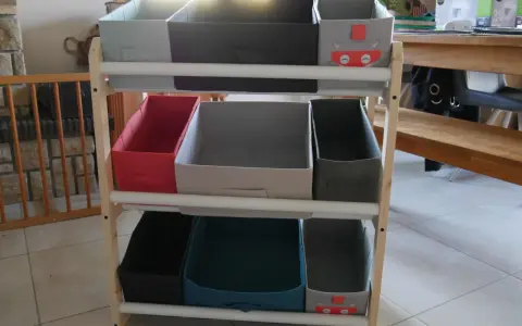 Étagère en bois avec des bacs de rangement pour jouets, dont un décoré d'un chat super-héros. Idéal pour fabriquer un rangement jouet organisé.