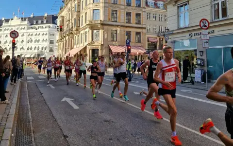 Corredores compiten en una media maratón en Europa, con edificios históricos y público animando.