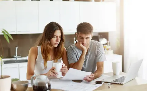 Couple pensif devant des papiers, peut-être une attestation d'assurance villégiature, dans une cuisine lumineuse.