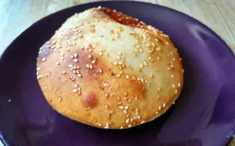 Bułka do hamburgerów posypana sezamem na fioletowym talerzu.