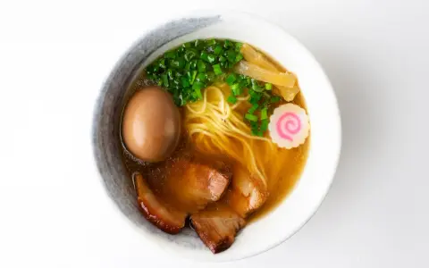 A miseczce shoyu ramen z makaronem, jajkiem, plastrami wieprzowiny, szczypiorkiem, bambusem i różową rybną kluską.