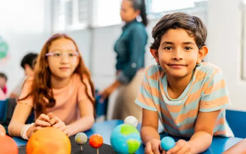 Kinder lernen spielerisch über das Sonnensystem. Ein Junge hält eine Himmelskugel, während ein Mädchen mit einem Modell des Sonnensystems experimentiert. Dies sind Beispiele für alternative Schulkonzepte.