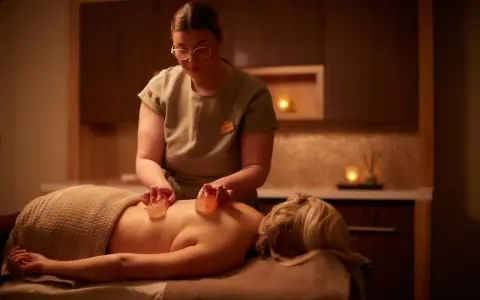 A therapist performs a Himalayan salt massage, placing warm salt stones on a client's back.