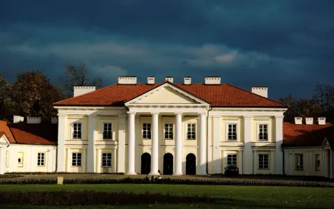 Pałac w Siedlcach, jedna z głównych atrakcji miasta, z charakterystycznym portykiem i czerwonym dachem, na tle burzowego nieba.