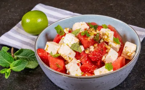 Erfrischender Wassermelonen-Feta-Salat mit Minze und Pinienkernen, garniert mit Limettenabrieb. Perfekt für heiße Tage.