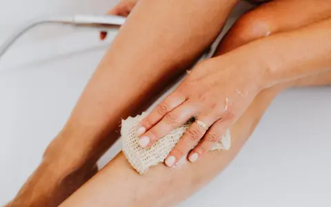 Une main utilise un gant de toilette pour exfolier sa peau, révélant une peau douce et lisse. C'est une étape clé pour savoir comment exfolier sa peau.