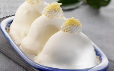 Tre deliziose delizie al limone, guarnite con panna e scorza di limone, in un piatto blu e bianco.