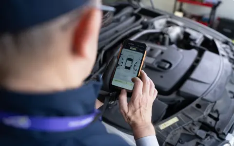 Mechanik sprawdza kody błędów DTC Renault na telefonie, analizując raport z pomiaru lakieru.