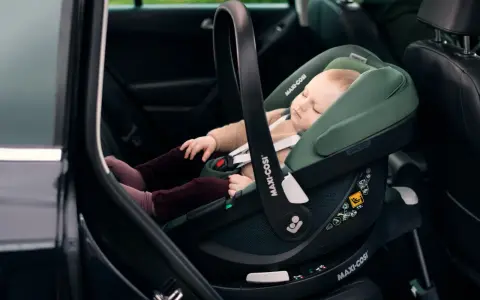 Schlafendes Baby in einer grünen Babyschale mit Isofix-Autobefestigung. Sicher und bequem auf Reisen.