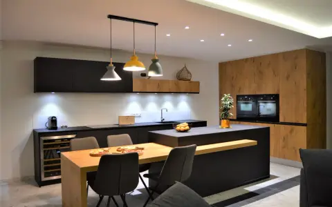 Une cuisine moderne aux accents beige et noir, avec un îlot central, des meubles en bois et des suspensions colorées.