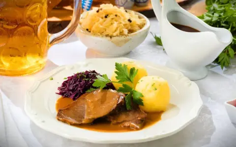 Deftiger Schweinebraten mit Klößen, Rotkohl und Sauerkraut. Dazu passt ein kühles Bier.