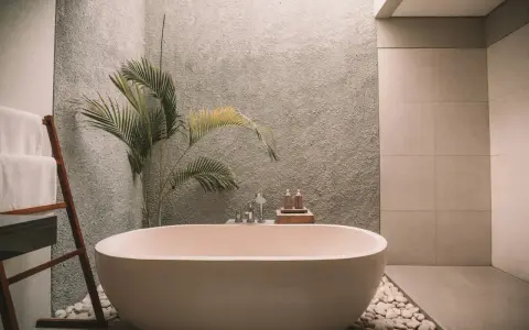Ett modernt badrum med fristående badkar, en grå texturerad vägg och en palm. Perfekt för att renovera badrum och skapa en spa-känsla.