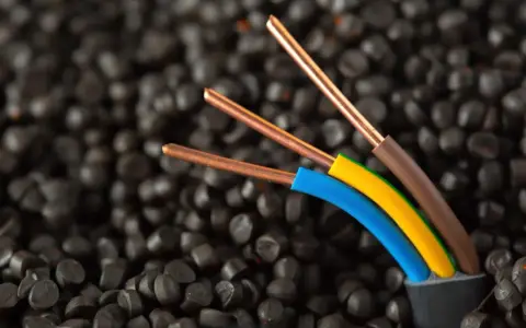 Trois fils électriques aux conducteurs en cuivre, dont un fil marron électrique, sortent d'un câble noir sur un fond de granulés noirs.