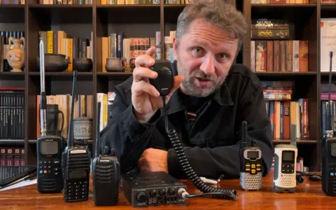 Mężczyzna prezentuje sprzęt CB radio, pokazując różne modele i akcesoria, które wpływają na zasięg.