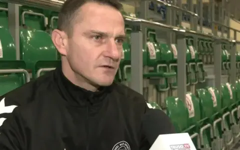 Marcin Pilch udziela wywiadu przed rzędem zielonych krzesełek na trybunach.