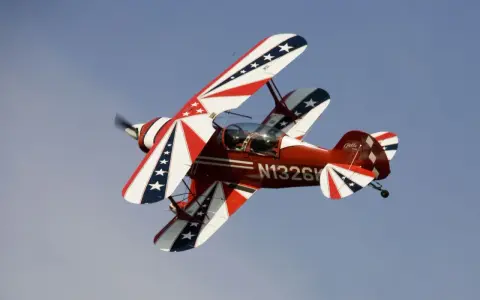 Rotes Pitts Special Doppeldeckerflugzeug mit Sternenmuster fliegt im blauen Himmel.