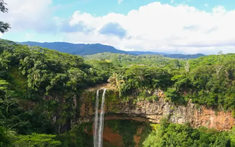 Majestatyczny wodospad na Mauritiusie spada kaskadami po skalnej ścianie, otoczony bujną, zieloną dżunglą i górami w tle.