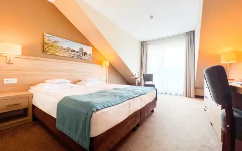 Przytulny pokój hotelowy z wygodnym łóżkiem, biurkiem i oknem. Idealne miejsce na nocleg tranzytowy, by odpocząć w podróży.