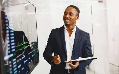 Un key account executive souriant présente des graphiques financiers sur un écran.