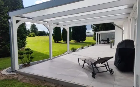 Moderne Terrasse bauen: Überdachter Sitzbereich mit Liegestuhl, Grill und Blick ins Grüne.
