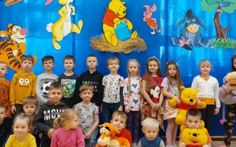 Dzieci pozują do zdjęcia z Kubusiem Puchatkiem i przyjaciółmi, świętując Dzień Kubusia Puchatka.