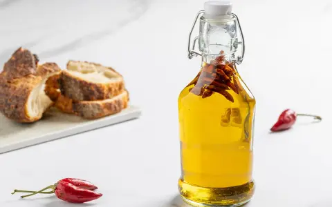 Olio al peperoncino in bottiglia, con peperoncini rossi e pane rustico a fette sullo sfondo.