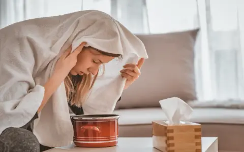 Une femme apprend comment faire une inhalation, la tête couverte d'une serviette au-dessus d'une casserole de vapeur.