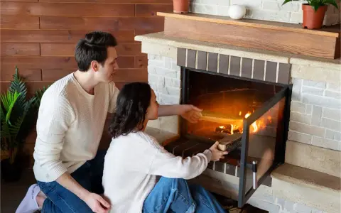 Pareja añade leña a la chimenea, creando un ambiente acogedor. Los insertables de madera se queman, iluminando la habitación.