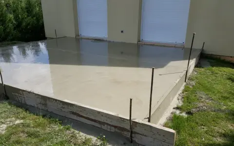 Une nouvelle dalle béton fraîchement coulée, prête à sécher. Les coffrages en bois et les fers à béton délimitent la zone.