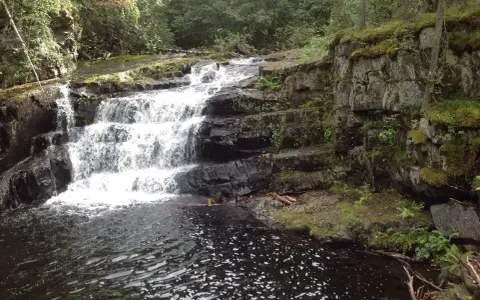 Vattenfall i en skogsmiljö nära Lillehammer, Norge. Mossbeklädda klippor och mörkt vatten.