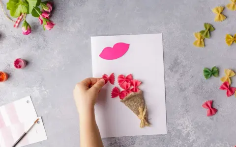 Manos creando flores manualidades con pasta de moño rosa, un ramo y labios de papel.