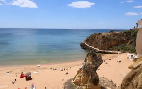 Sonniger Lagos Strand mit goldenem Sand, türkisfarbenem Wasser und Felsformationen. Menschen entspannen sich, spielen und genießen die Aussicht.
