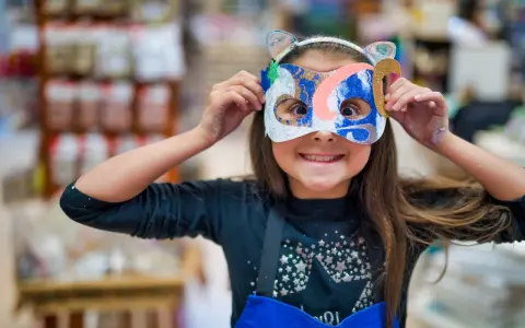 Une jeune fille, le visage caché par un masque coloré, explore la symbolique du visage et la joie de la transformation.