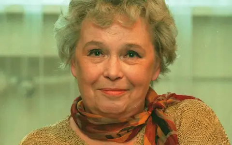 Uśmiechnięta Joanna Chmielewska, autorka kultowych powieści kryminalnych, w beżowym swetrze i kolorowym szalu.