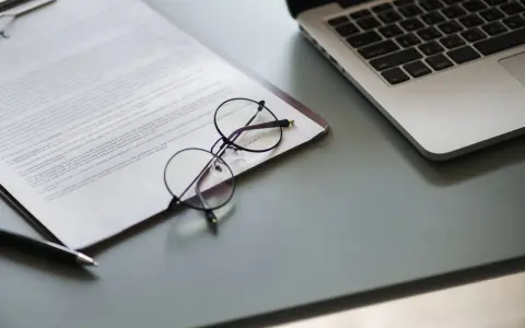 Okulary na dokumencie z tekstem, obok laptopa. Dokument może zawierać pełnomocnictwo lub strategię marketingową.