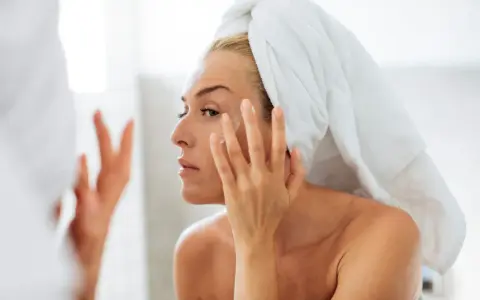 Une femme, serviette sur la tête, applique une crème sur son visage. Un geste essentiel pour prendre soin de sa peau en hiver.