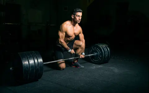 Un homme musclé s'apprête à soulever une barre chargée, profitant d'un temps de repos musculation dans une salle sombre.