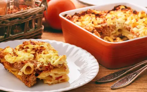 Zapiekanka makaronowa z mięsem mielonym w sosie śmietanowym, podana na talerzu i w naczyniu żaroodpornym.