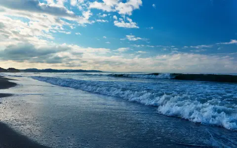 Plaża nad Bałtykiem z falami i błękitnym niebem z chmurami.