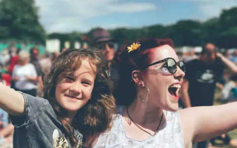 Zwei lachende Frauen, eine davon ein Kind, genießen das vivawest family festival. Glitzer auf den Wangen und eine Blume im Haar.