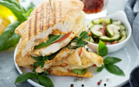 Pyszne panini z kurczakiem, pomidorem i bazylią, podane z sałatką z ogórka. Idealne na lekki lunch.