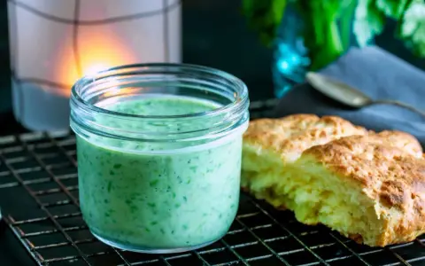 En burk med krämig, grön dressing, perfekt för ett grönt gudinnedressing recept. Bredvid ligger nybakade scones.