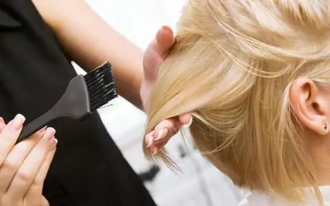 Fryzjerka wykonuje konturowanie włosów blond, nakładając farbę pędzelkiem.