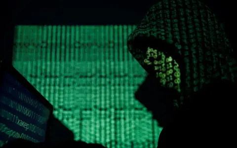 A hooded figure works on a laptop, bathed in the green glow of binary code. This scene evokes the shadowy world of China cyber espionage.