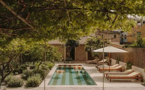 Piscina con galleggianti in un giardino rigoglioso, perfetto per idee piccoli giardini con piscina. Lettini e ombrellone invitano al relax.