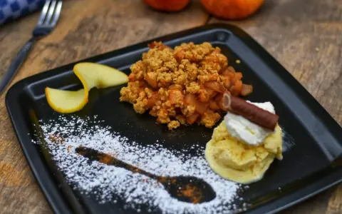 Ein köstlicher Apfel Crumble mit Haferflocken, serviert mit Vanilleeis, Sahne und einem Schokostäbchen.