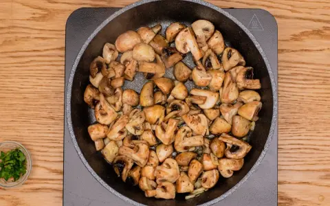Champiñones al ajillo dorándose en una sartén, con perejil picado en un cuenco al lado.