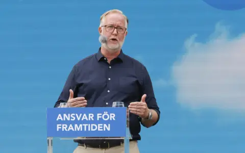 Man med glasögon och mikrofon talar vid ett podium med texten "Ansvar för framtiden". Hans gestik och budskap speglar en liberalism ideologi.