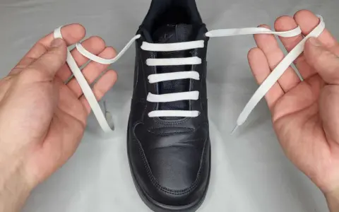Mani che mostrano come mettere i lacci alle scarpe senza fiocco, con un laccio bianco che attraversa gli occhielli di una scarpa nera.