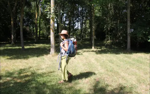 Une randonneuse avec un sac à dos et une poche à eau visible. Elle est dans une forêt, prête pour son aventure.